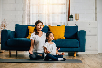 Family yoga at home. A beautiful mother and her charming daughter smile while practicing yoga in...