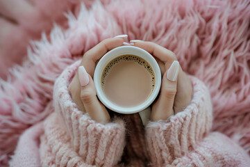 hands holding a cup of coffee, pink knit sweater and fuzzy pink blanket