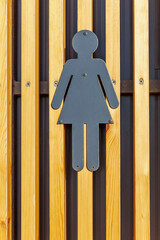 Metal gray women's toilet icon on a wooden slatted wall. Identification of the rest room. Front...