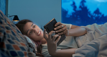 Indian Asian Hindu gen z upset sad alone young woman lady crying lying on bed use mobile check sms late night indoor home. Lonely female girl hold phone look screen read bad cyber text room house