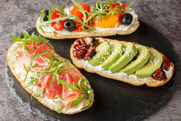 Set of open toasted bruschetta with arugula, jamon, vegetables, cream cheese close-up on a slate board on the table. Horizontal