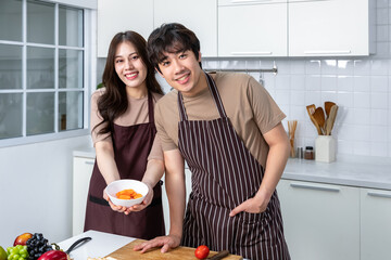Young Asian couple male man female woman cheerful standing and preparing food for meal, enjoy cooking, in kitchen at home.