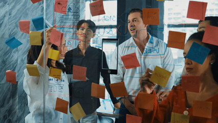 Portrait of professional business team brainstorming marketing idea by using sticky notes to share creative idea at glass wall. Group of diverse business team discuss about strategy. Manipulator.