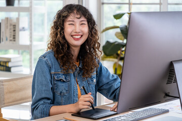 Portrait of young Asian female woman businessperson graphic designer working, creating, and using computer in office. Looking at camera.