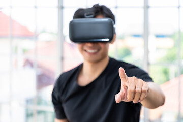 Asian male man wearing VR google headset using virtual reality in living room at home. Pointing or touching.