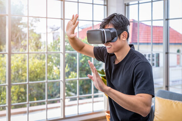 Asian male man wearing VR google headset using virtual reality in living room at home