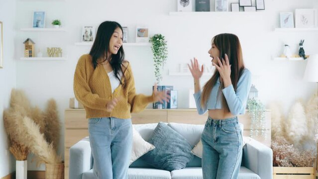Two asian young woman recording trend dance video on smartphone in living room. Overjoyed teen girl dancing to favorite energetic music, having fun with joyful