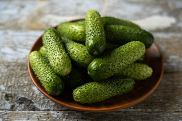 Green cucumbers on a plate, old wooden background