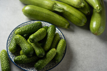 Fresh cucumbers on a plate, zucchini in the background, light gray stone background, horizontal format