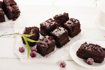 Chocolate cake with cherry cut into pieces, white wooden background, coffee with milk in the foreground