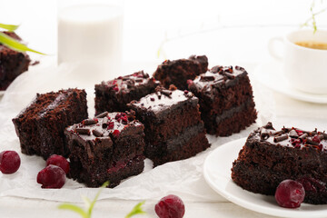 Chocolate cake with cherry cut into pieces, white wooden background, coffee with milk in the foreground
