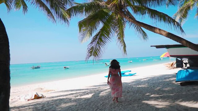 Indian Woman walking barefoot on white sand beach at Agatti Island, Lakshadweep, India. Woman on tropical beach Lakshadweep island. Young woman walking at beach under coconut tree. Summer Holidays.