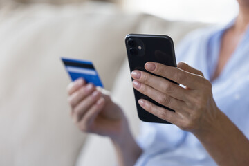 Secure e-payment, electronic commerce, ecommerce client makes on-line purchases. Close up unknown female hands holding debit card and smartphone, do online shopping, transfer money through mobile app