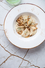 Plate with vareniki dumplings and caramelized onion, flat lay on a white granite background, vertical shot