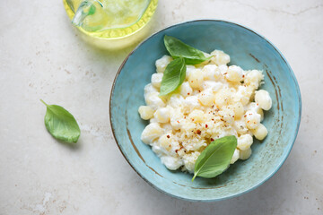 Plate of chicche di patate with cheese sauce and green basil, horizontal shot on a light-beige stone background, elevated view