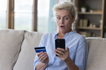Worried surprised elderly woman holding card, look at smartphone, feels stressed, bad online bank...