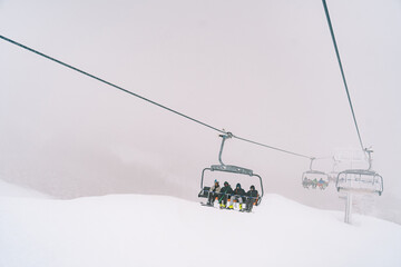 Skiers on chairlift ride up a foggy snowy slope