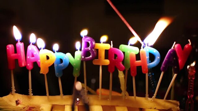 Somebody lights coloured happy birthday candles by taper on cake.