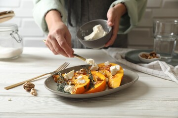 Woman putting cheese on baked pumpkin slices at table, closeup