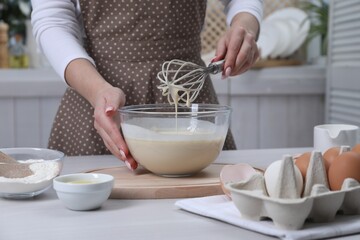 Woman making dough with whisk in bowl at table, closeup