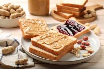 Delicious toasts with peanut butter, jam and nuts on light wooden table, closeup