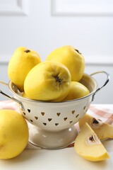 Tasty ripe quinces and metal colander on white wooden table