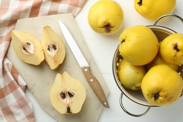 Tasty ripe quinces, metal colander and knife on white wooden table, flat lay