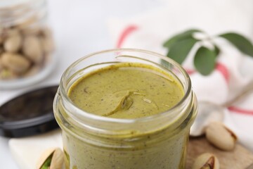 Obraz na płótnie Canvas Tasty pistachio cream in jar on blurred background, closeup