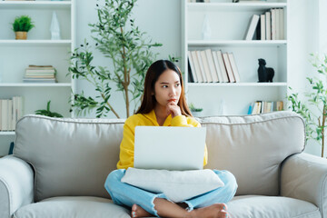 Happy young Asian woman using laptop while seated on couch at home