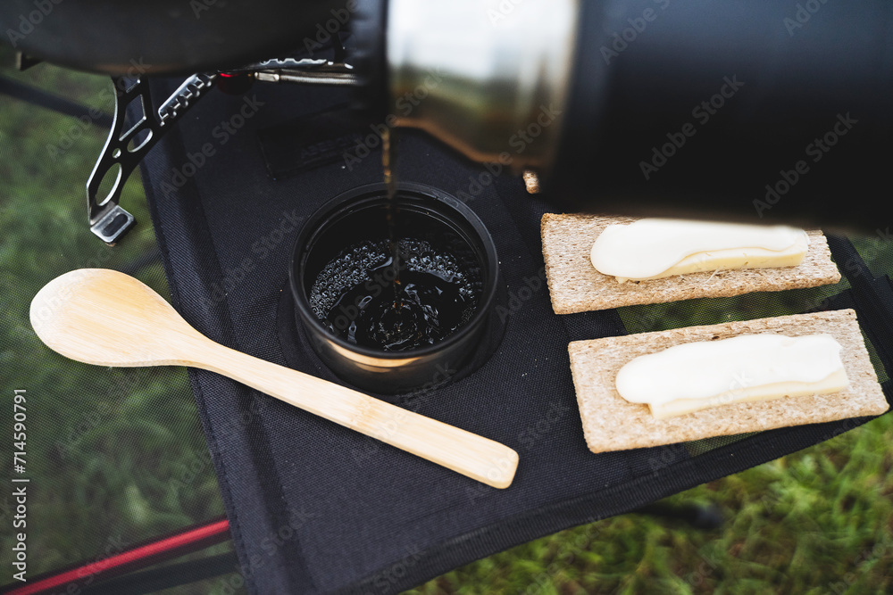 Sticker Pour hot tea from a thermos into a glass, a view of the pouring water on top of a mug, a wooden spoon on the table, butter sandwiches, food on a hike.