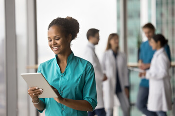 Cheerful young African American medical worker using online healthcare application on tablet for job, reading patients records, checkup test electronic result, online content, smiling