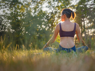 Young asian woman doing meditation in morning or evening at park, healthy woman relaxing and practicing yoga at city park. Mindfulness, destress, Healthy habits and balance concept