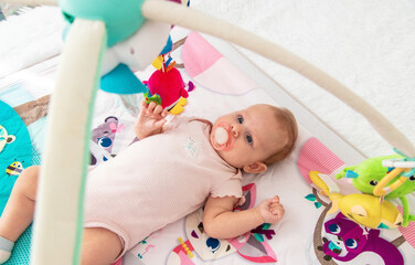 a baby plays with hanging toys on a play mat. a child, a baby plays at home
