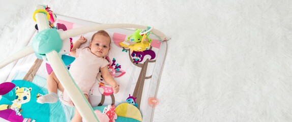 a baby plays with hanging toys on a play mat. a child, a baby plays at home - obrazy, fototapety, plakaty