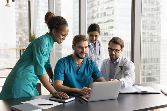 Diverse team of positive successful medical professionals using internet communication on laptop, meeting at computer together, discussing healthcare technology, looking at display, talking