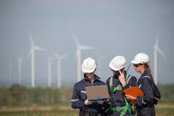 Team of engineers working and using a computer laptop on site in wind turbine farm, Wind turbines...