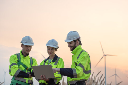 Team of engineers working and using a computer laptop on site in wind turbine farm, Wind turbines generate clean energy source, Eco technology for electric, industry environment
