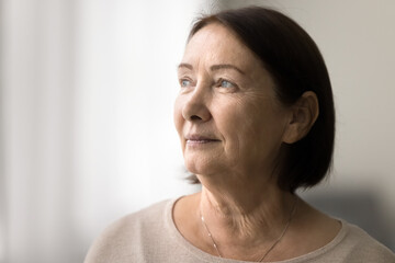 Fototapeta premium Serious pensive senior woman close up casual portrait with copy space. Thoughtful face of elderly female model looking at window away, daydreaming, thinking, pondering