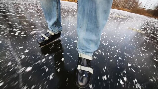 Legs of man in jeans skating on frozen pond among trees