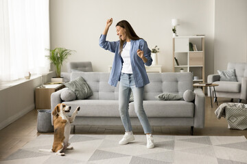 Cheerful excited dog owner woman dancing with smart funny pet at home, having fun, training trick...