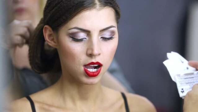 Makeup artist glues false eyelashes while other makes hairdo to model