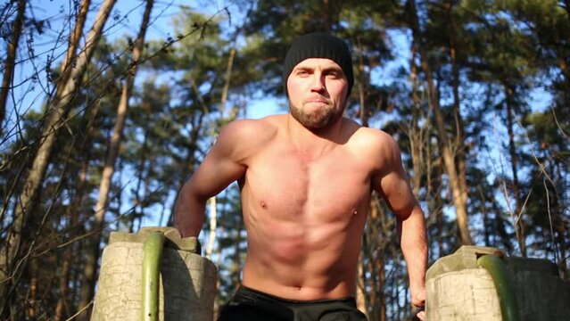 Young half-naked man does exercise on parallel bars in park