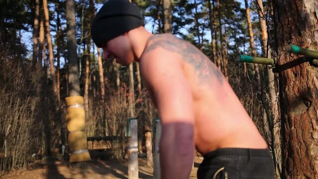 Young half-naked man moves large heavy tire in sunny forest