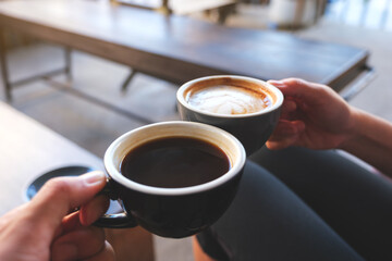 Closeup image of a couple people clinking coffee mugs in cafe