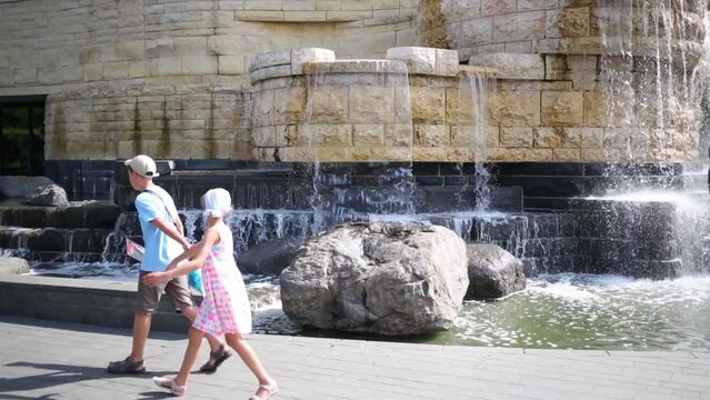 Two children play near beautiful fountain in city at summer