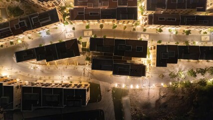 Aerial night view of an illuminated urban street with buildings and trees, creating a serene and atmospheric cityscape