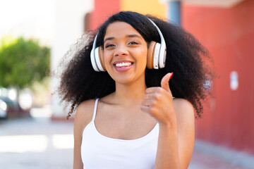 Young African American woman at outdoors listening music and with thumb up