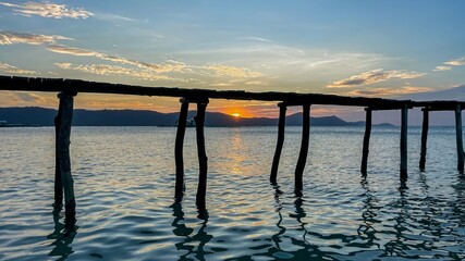Tranquil seascape with wooden pier silhouette against a stunning sunset background, reflecting on calm ocean waters