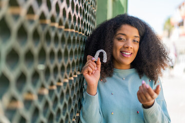 Young African American woman holding invisible braces at outdoors inviting to come with hand. Happy...