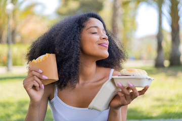 Young African American woman at outdoors holding a burger and fried chips with happy expression